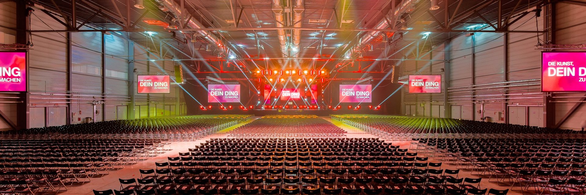 Halle 2 - Christian Bischoff - DIE KUNST, DEIN DING ZU MACHEN mit Reihenbestuhlung und Bühne mit Bildschirmen und Lichtinstallation, © Christian Bischoff LIFE GmbH